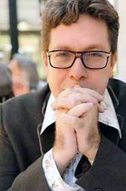 Head shot photo of former literary agent Mark Malatesta with glasses, floral shirt, and brown jacket