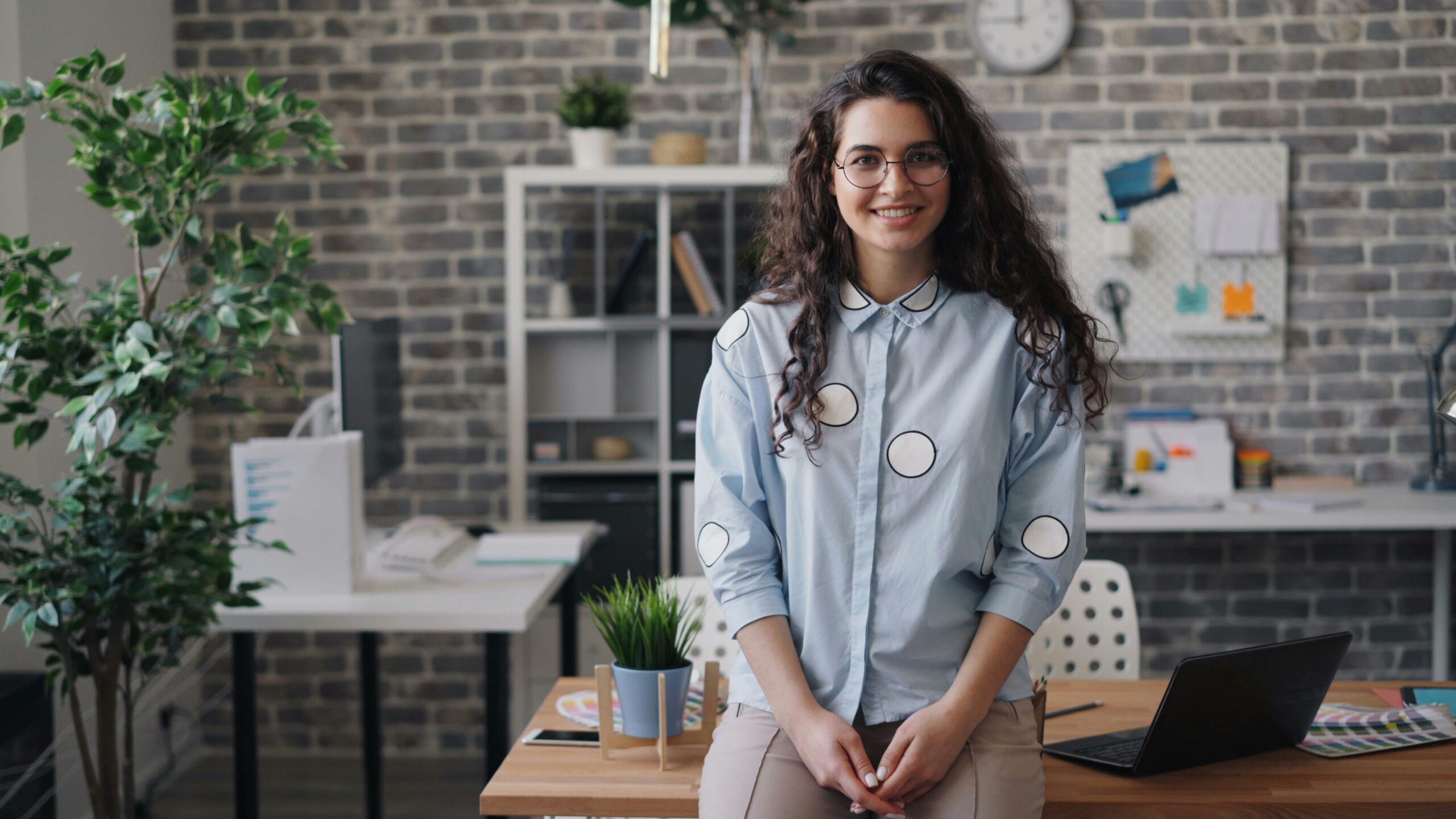 Smiling young woman standing confidently in a modern office workspace.